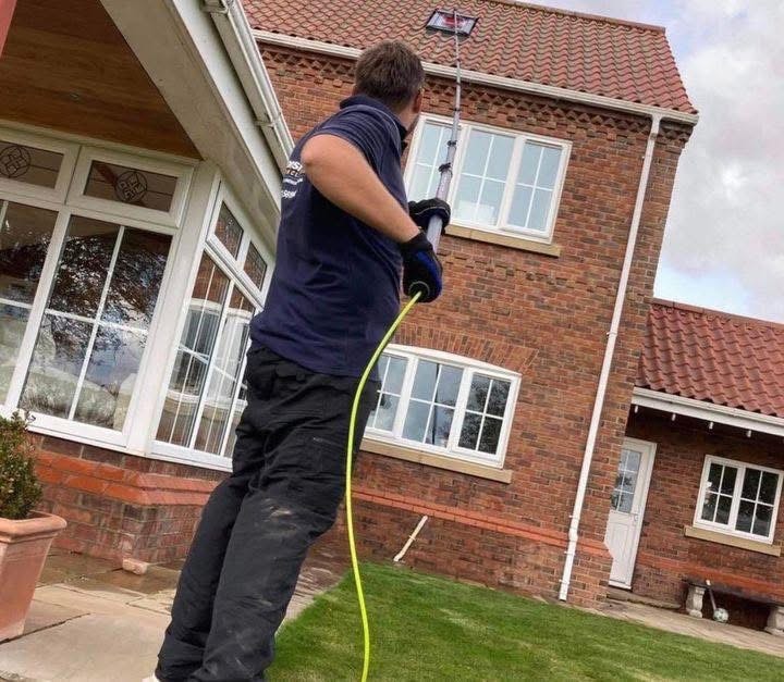 Window cleaner using water-fed pole to clean Velux windows on detached brick home in Lincolnshire